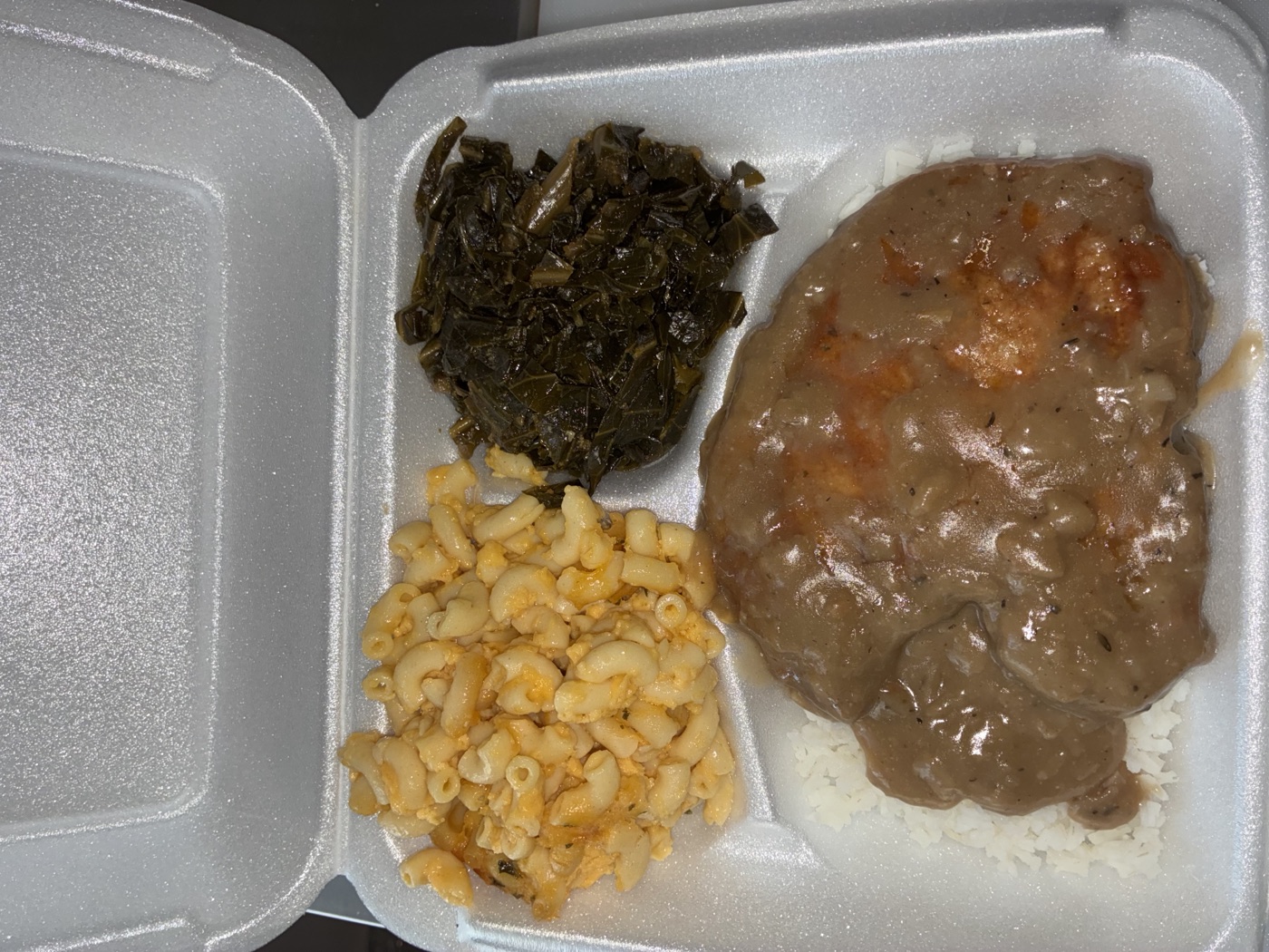 Smothered Pork Chop plate served over rice with collard greens and mac & cheese